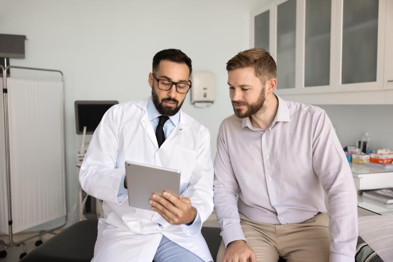 Confident doctor holding digital tablet explaining male patient medical data