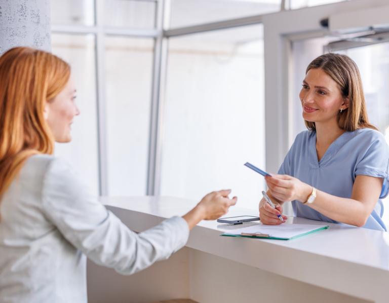 Female patient receiving appointment card at medical clinic reception desk