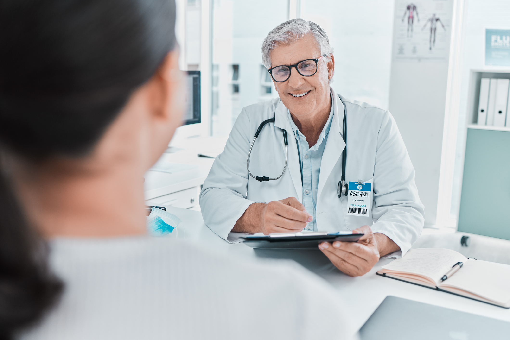 Shot of a mature doctor sitting with his patient and holding a clipboard during a consultation in his clinic