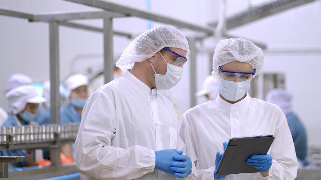 Engineers control quanlity and process of production by application on tablet, discussing project work about production plan at manufacturing storage. production line worker in white sterile uniforms working together in manufacturing plants. Teamwork.