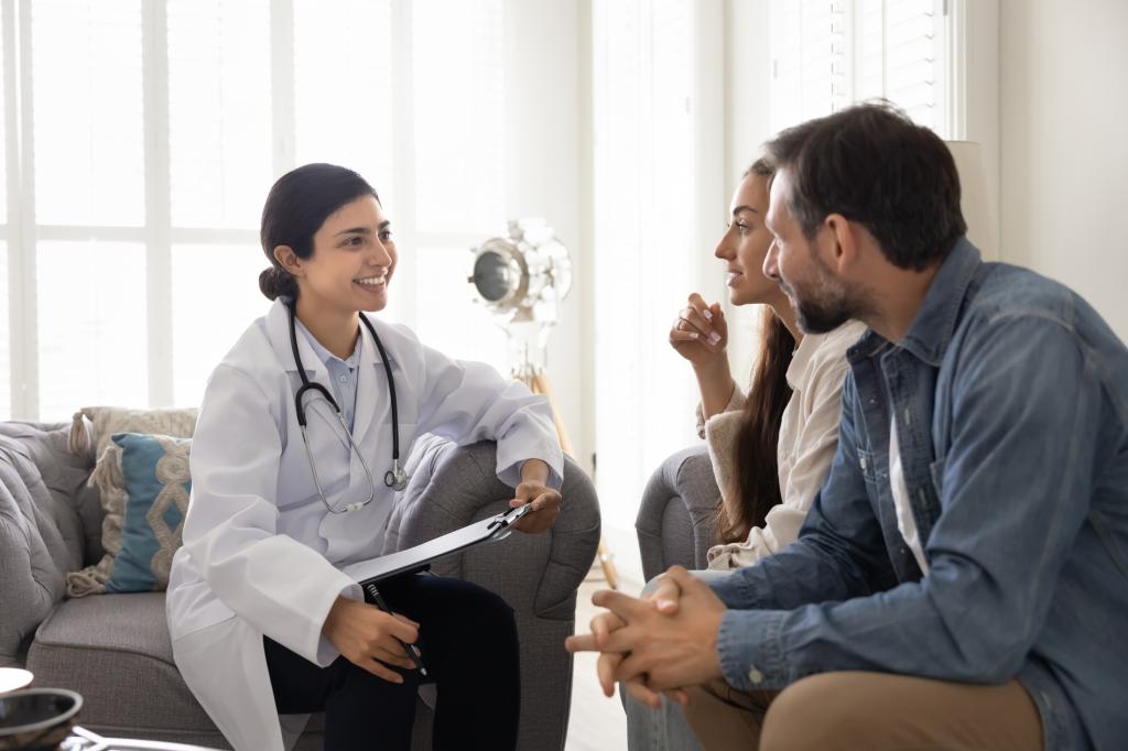 Young smiling Indian doctor listening married couple during medical meeting